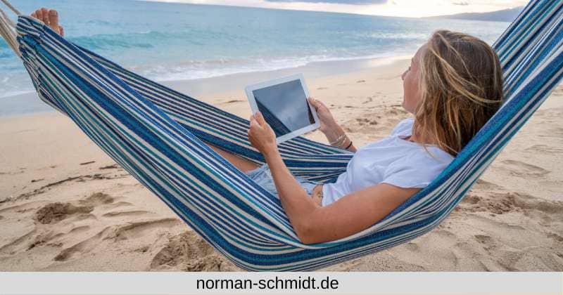 Frau in Hängematte am Strand die mit Ihrem Tablett als digitaler Nomade ihrer Tätigkeit im Affiliate Marketing nachgeht